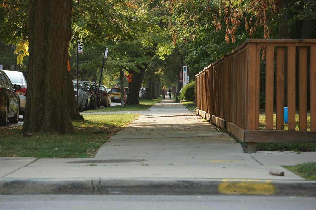 A quiet suburban street with a sidewalk and wooden fence