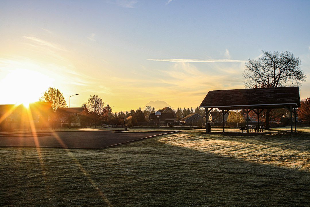 the sun is setting over a park with a gazebo